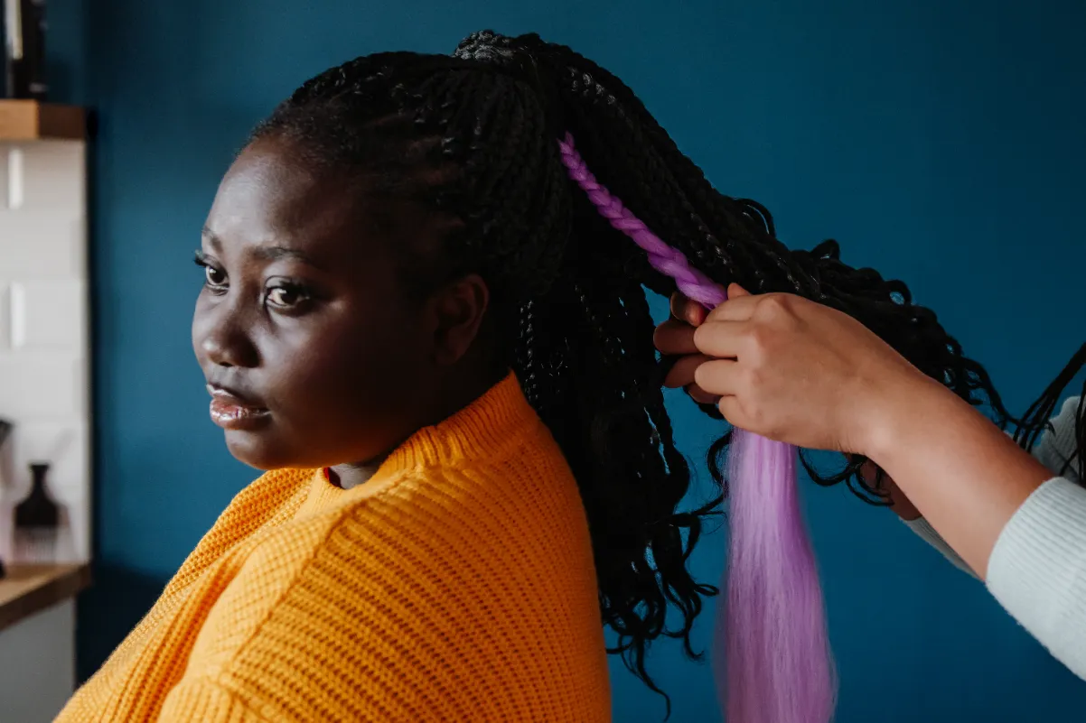 A woman getting her hair braided with some colorful highlights.